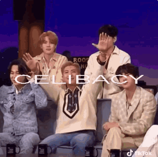 One of the members of Korean Pop band BTS standing up from the couch at the stage of James Cordon's show with the word 'celibacy' on the screen.